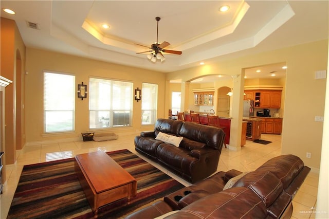 tiled living room featuring ceiling fan, beverage cooler, and a tray ceiling