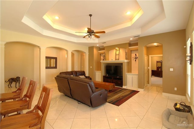 tiled living room with a tray ceiling, ceiling fan, and ornate columns