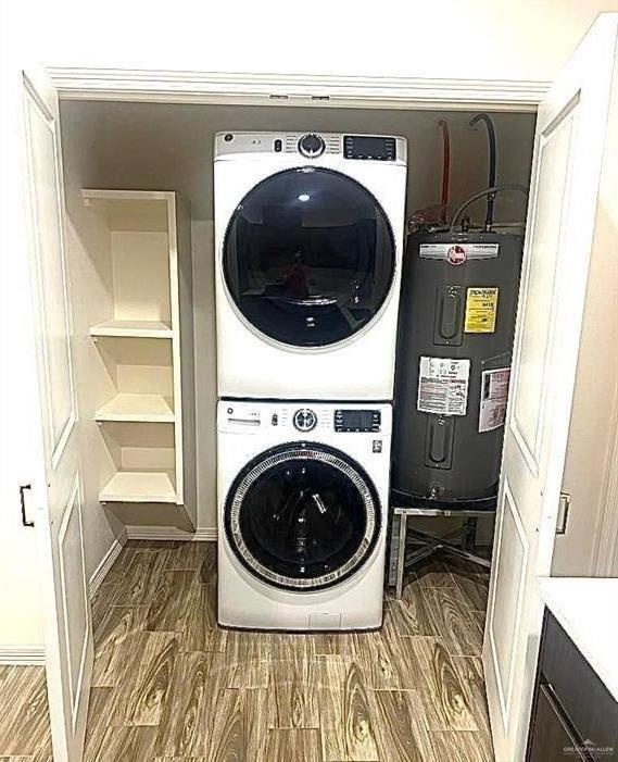 laundry room featuring wood-type flooring, electric water heater, and stacked washer and clothes dryer