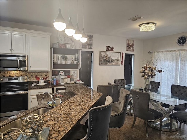 kitchen with white cabinets, stainless steel appliances, hanging light fixtures, and dark stone counters