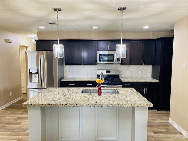 kitchen with light hardwood / wood-style flooring, pendant lighting, stainless steel appliances, and a kitchen island with sink