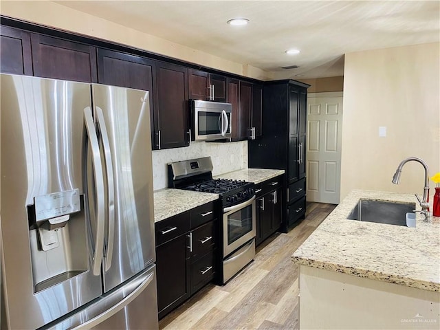 kitchen with light hardwood / wood-style flooring, sink, backsplash, stainless steel appliances, and light stone countertops