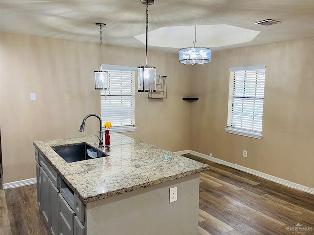 kitchen featuring an island with sink, light stone counters, pendant lighting, sink, and dark hardwood / wood-style floors