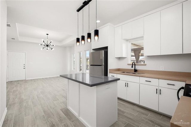 kitchen with white cabinets, a raised ceiling, sink, hanging light fixtures, and stainless steel fridge