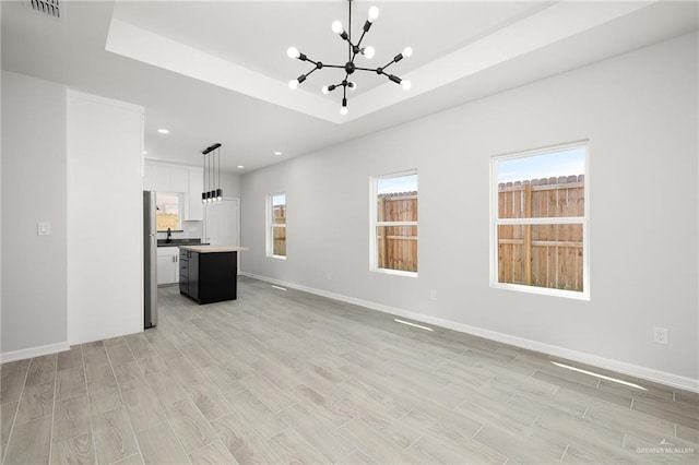 unfurnished living room with a notable chandelier, plenty of natural light, and a tray ceiling