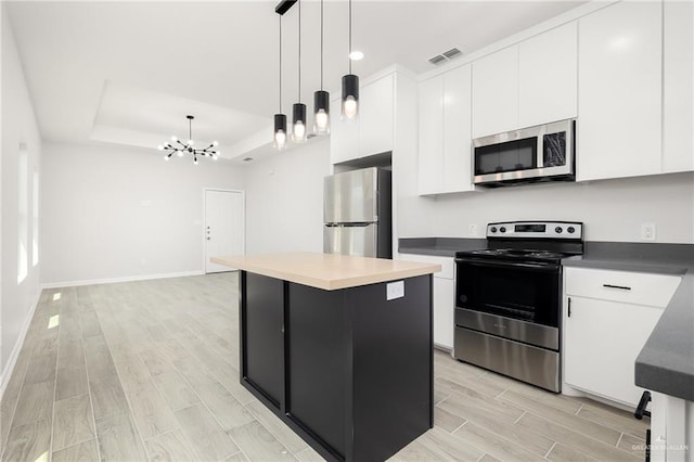 kitchen featuring a center island, stainless steel appliances, an inviting chandelier, pendant lighting, and a tray ceiling