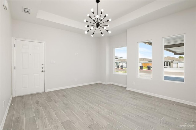 spare room featuring a raised ceiling, a chandelier, and light wood-type flooring