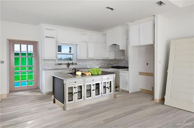 kitchen with backsplash, light hardwood / wood-style flooring, white cabinets, and a kitchen island