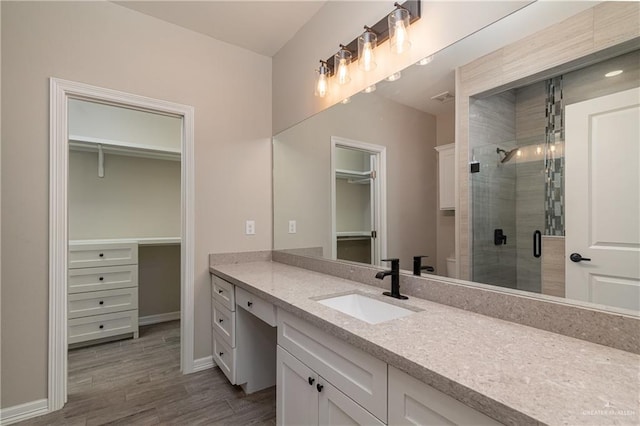 bathroom with a stall shower, a spacious closet, vanity, and wood finished floors