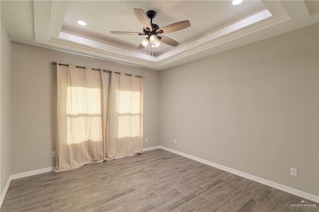 spare room featuring a tray ceiling, wood finished floors, a ceiling fan, and baseboards