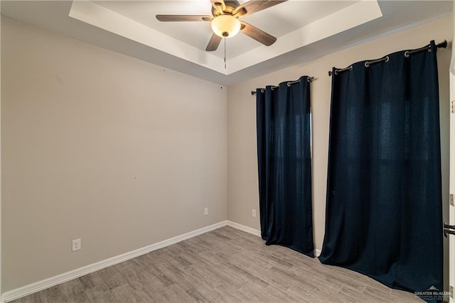 spare room featuring light wood-style flooring, baseboards, a raised ceiling, and a ceiling fan