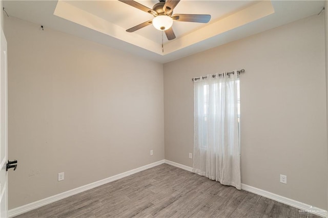 spare room with a tray ceiling, wood finished floors, a ceiling fan, and baseboards