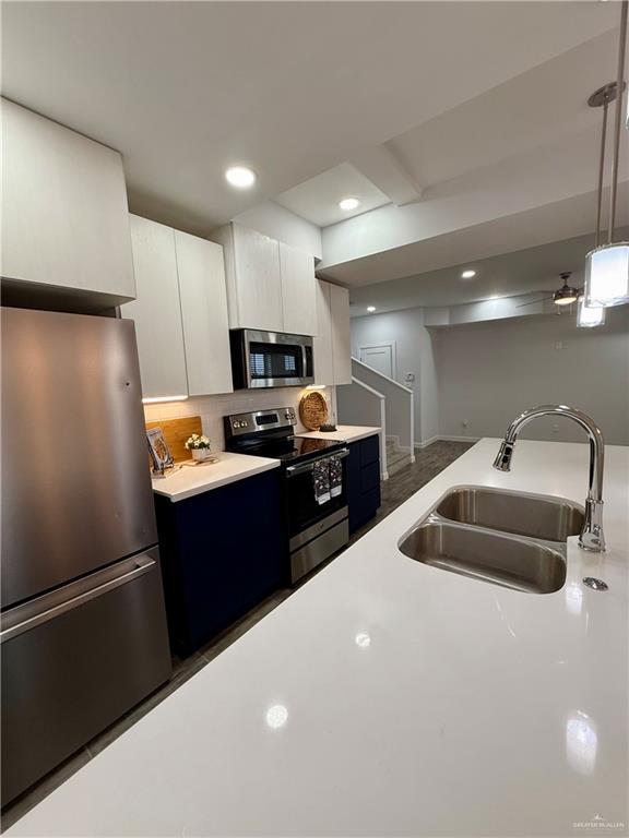 kitchen with light countertops, white cabinetry, a sink, decorative light fixtures, and stainless steel appliances