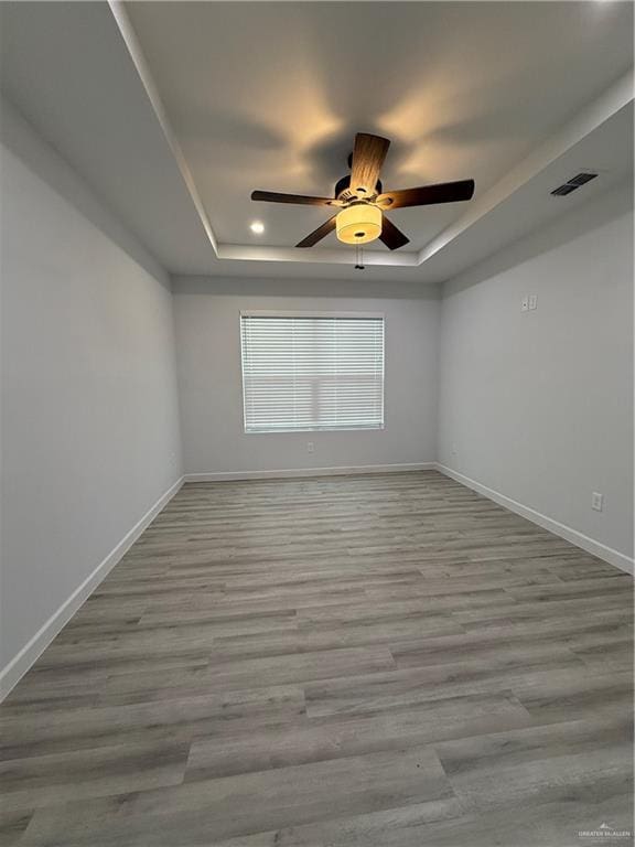unfurnished room with visible vents, a ceiling fan, baseboards, and a tray ceiling