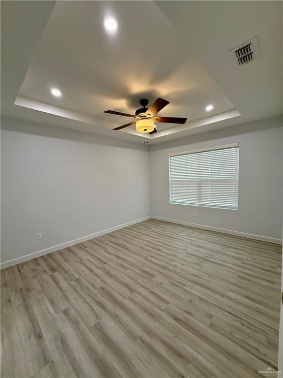 spare room featuring light wood-style flooring, recessed lighting, a ceiling fan, a tray ceiling, and visible vents
