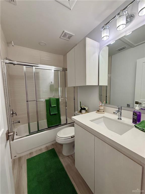 bathroom featuring toilet, visible vents, combined bath / shower with glass door, and wood finished floors