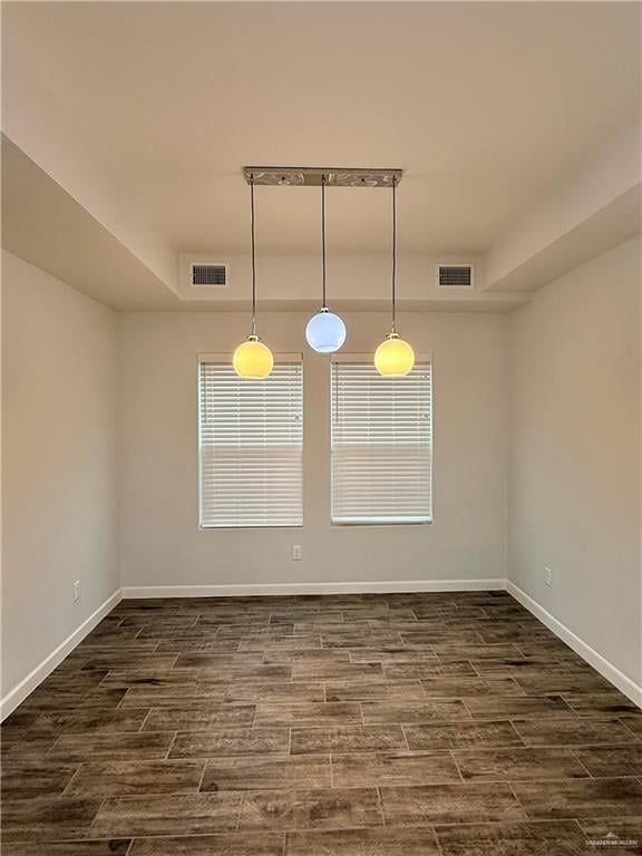 empty room with dark wood-style flooring, a tray ceiling, visible vents, and baseboards