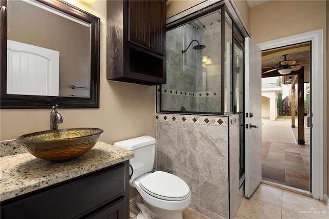 bathroom featuring ceiling fan, tile patterned flooring, a tile shower, vanity, and toilet