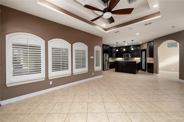 kitchen with a tray ceiling, light tile patterned flooring, stainless steel appliances, and a center island with sink