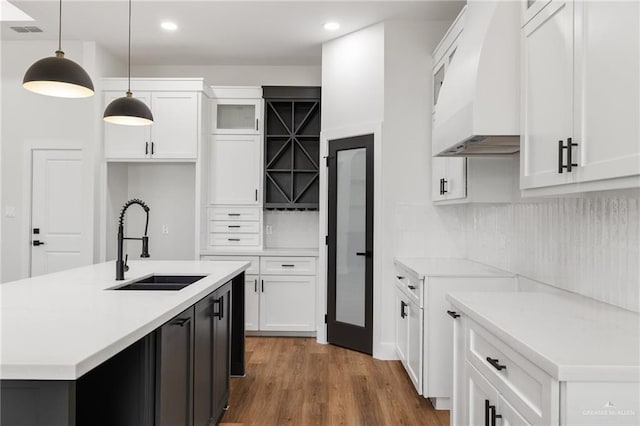 kitchen featuring decorative light fixtures, premium range hood, sink, white cabinetry, and a kitchen island with sink