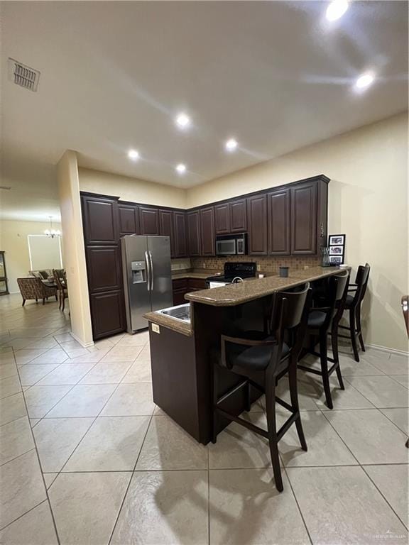 kitchen with a kitchen breakfast bar, kitchen peninsula, appliances with stainless steel finishes, tasteful backsplash, and dark brown cabinetry