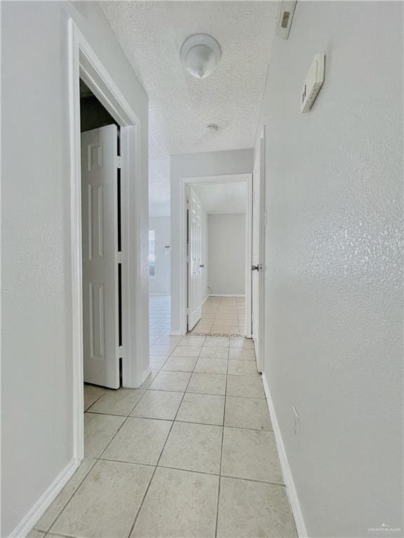 hall featuring a textured ceiling, baseboards, and light tile patterned floors