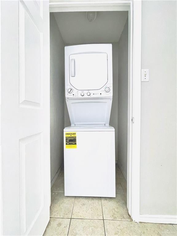 laundry room with laundry area, light tile patterned floors, baseboards, and stacked washer and clothes dryer