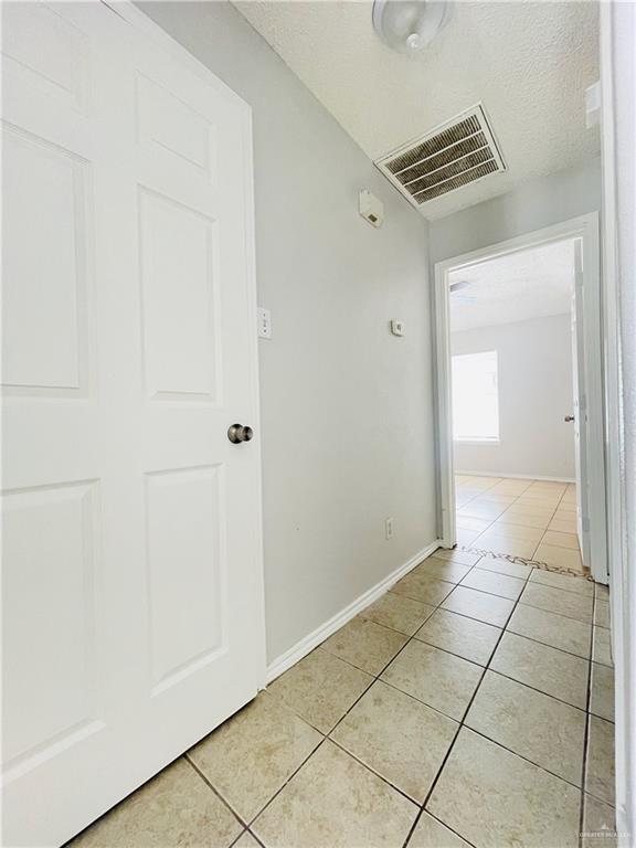 hallway with visible vents, a textured ceiling, baseboards, and light tile patterned flooring