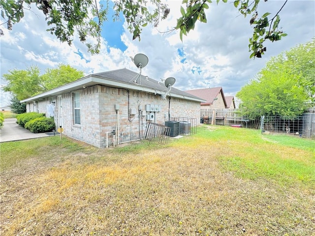 rear view of house featuring a yard, brick siding, fence, and central air condition unit