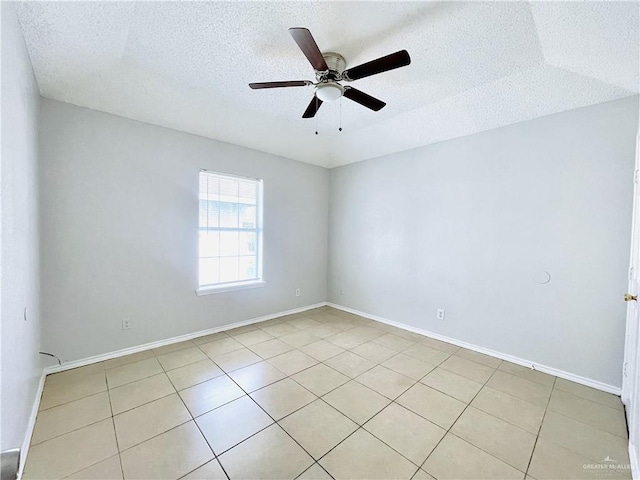 spare room with a textured ceiling, light tile patterned flooring, a ceiling fan, and baseboards