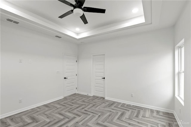 spare room with ceiling fan, a tray ceiling, and light parquet flooring