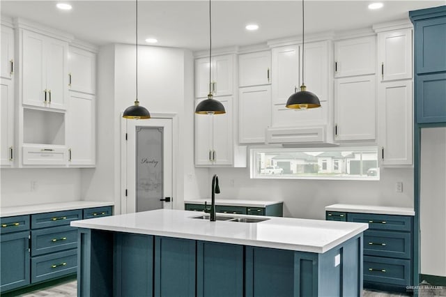 kitchen featuring white cabinetry, sink, decorative light fixtures, and a center island with sink