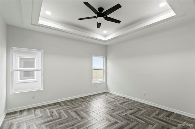 empty room with a raised ceiling, ceiling fan, and dark parquet floors