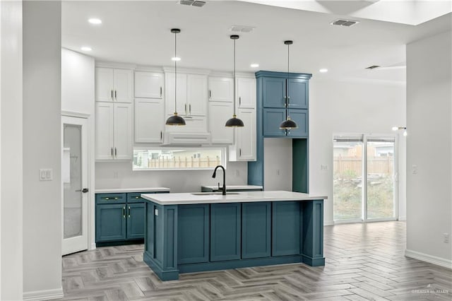 kitchen featuring white cabinetry, sink, hanging light fixtures, light parquet floors, and a kitchen island with sink