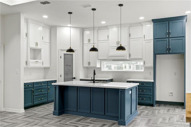 kitchen with pendant lighting, sink, white cabinetry, and an island with sink