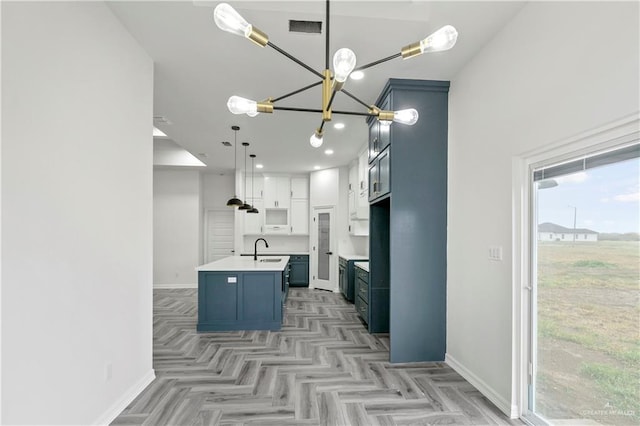 kitchen featuring decorative light fixtures, white cabinetry, sink, light parquet flooring, and a center island with sink