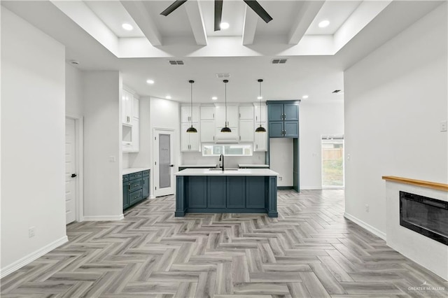 kitchen with sink, blue cabinets, a center island with sink, decorative light fixtures, and light parquet flooring