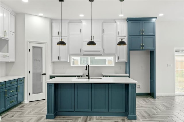 kitchen with light parquet flooring, hanging light fixtures, sink, and a center island with sink