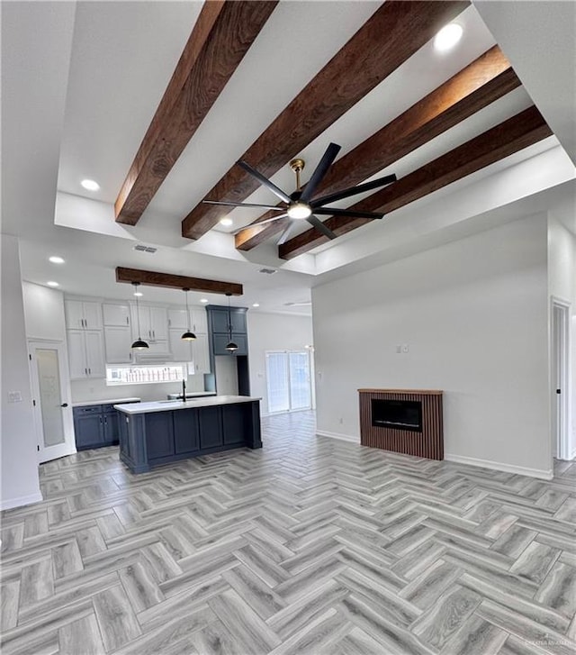 interior space with blue cabinetry, a breakfast bar, white cabinetry, a center island with sink, and beamed ceiling