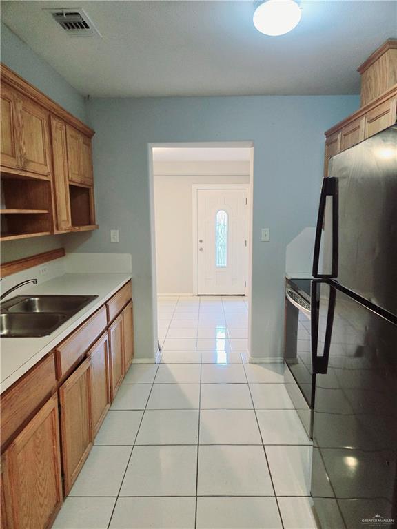 kitchen featuring sink, light tile patterned floors, stainless steel electric range, and refrigerator