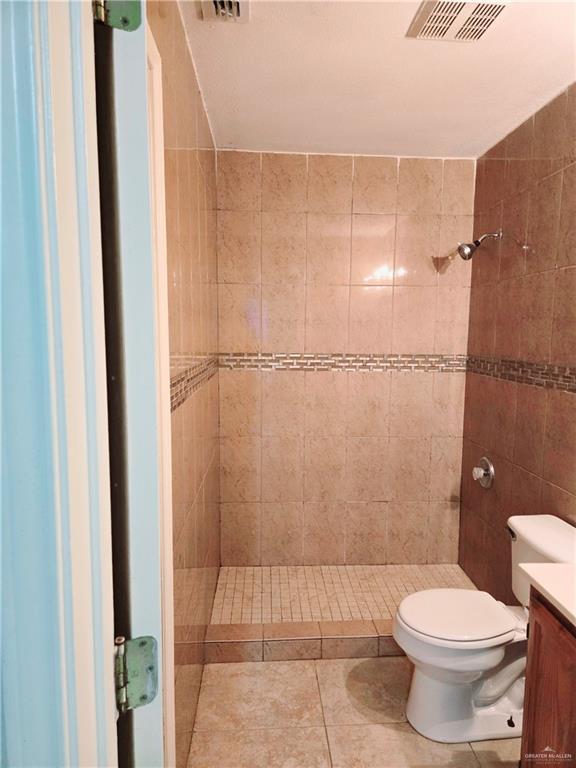 bathroom featuring tile patterned floors, vanity, toilet, and a tile shower