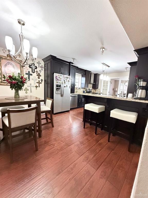 kitchen with light wood finished floors, appliances with stainless steel finishes, a peninsula, pendant lighting, and a notable chandelier