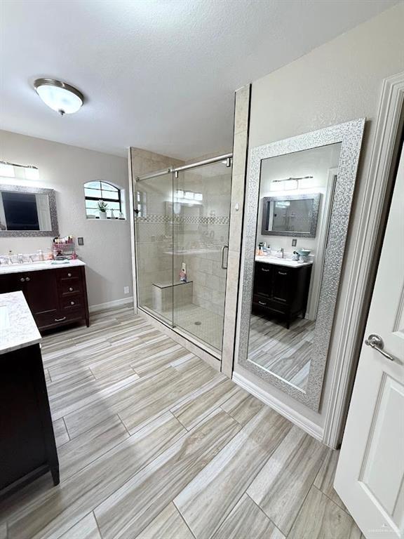 full bathroom featuring a shower stall, a textured ceiling, two vanities, and wood finish floors