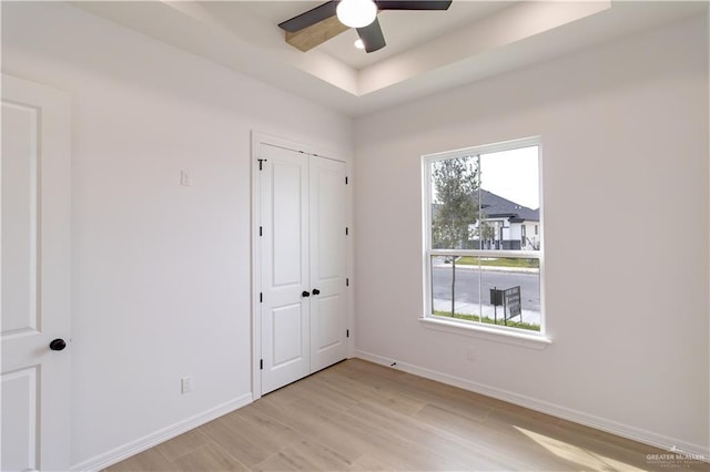 unfurnished bedroom with light wood-style flooring, a tray ceiling, baseboards, and ceiling fan