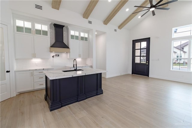 kitchen featuring premium range hood, beam ceiling, a sink, light wood-type flooring, and backsplash