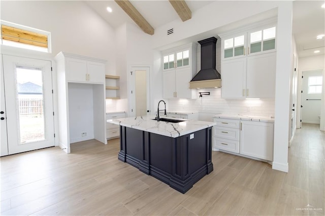 kitchen with beam ceiling, a sink, custom range hood, white cabinets, and tasteful backsplash