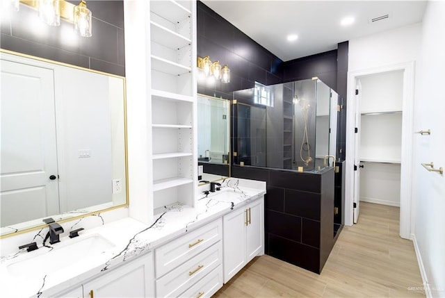 full bath with double vanity, a stall shower, a walk in closet, and a sink