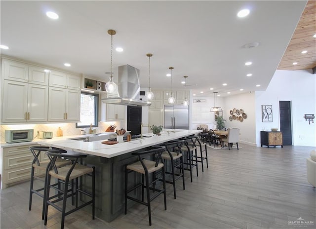 kitchen with a spacious island, hanging light fixtures, hardwood / wood-style flooring, appliances with stainless steel finishes, and island range hood