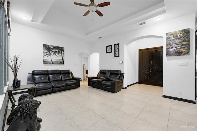 living room featuring a raised ceiling, ceiling fan, and light tile patterned flooring