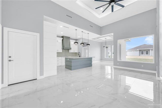 unfurnished living room with sink, a tray ceiling, ceiling fan, and a towering ceiling